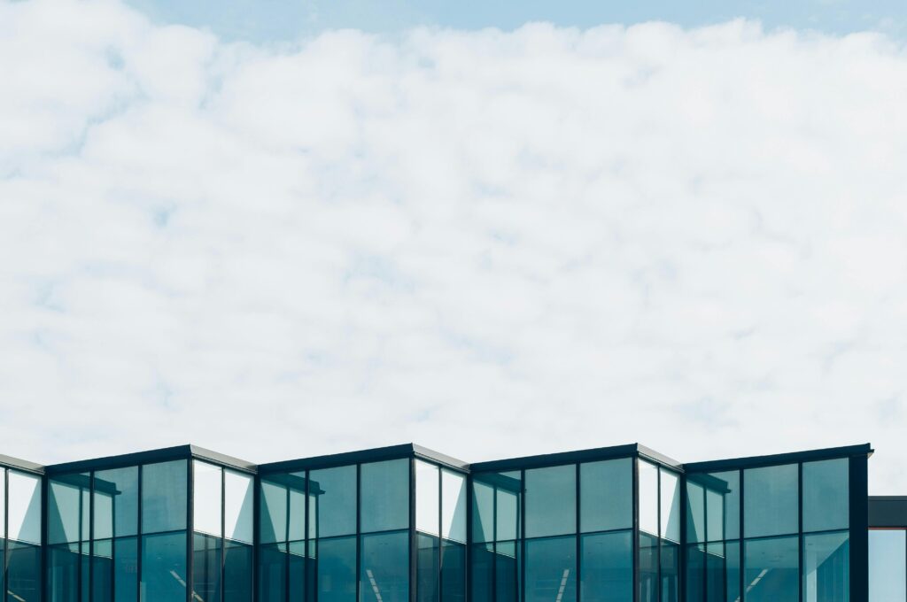 Low angle view of a modern glass building with a cloudy sky background, showcasing contemporary architecture.